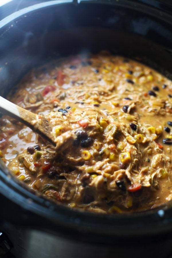 Queso Crockpot Chicken Chili in a crockpot with a wooden spoon.