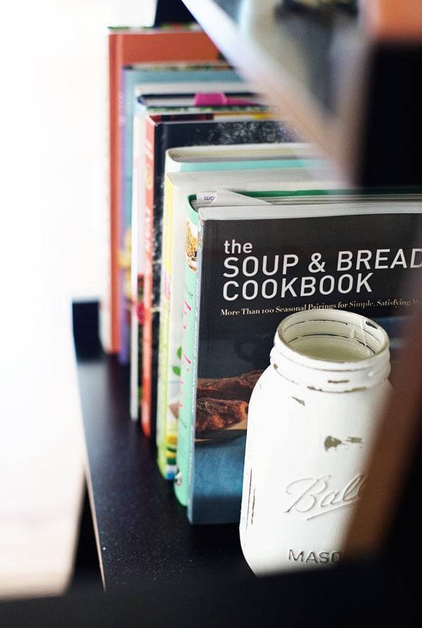 Painted mason jar holding cookbooks on a shelf.