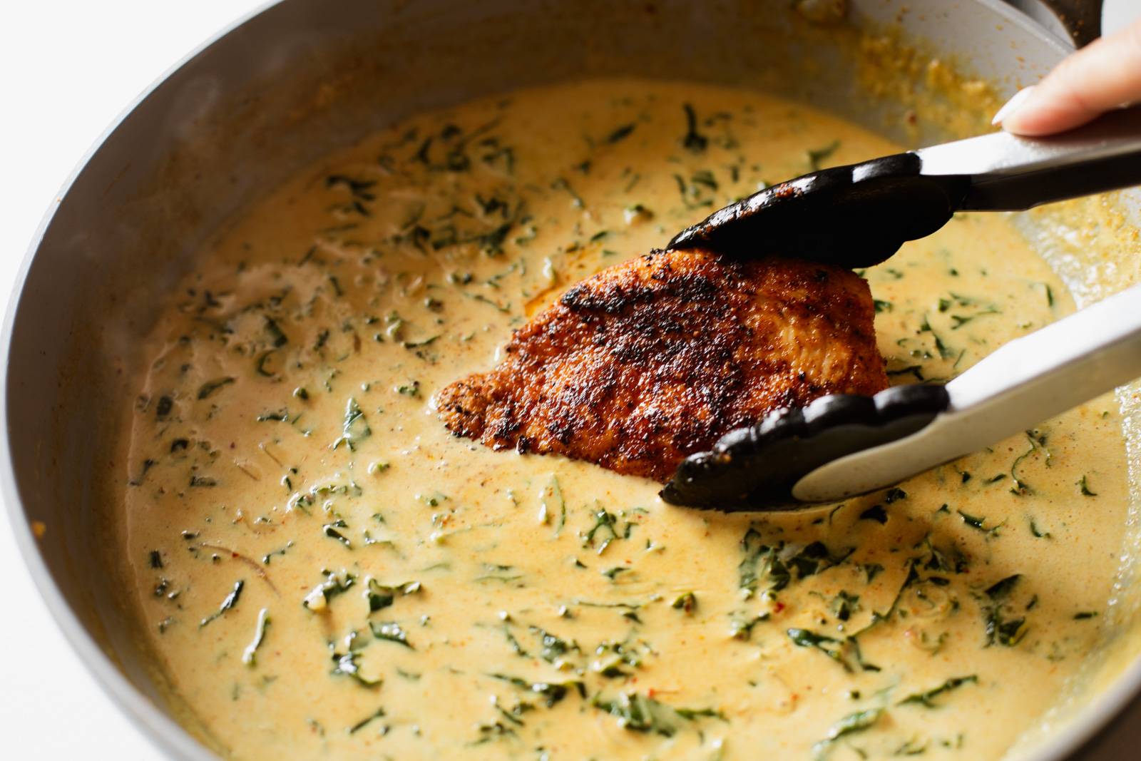 Placing chicken in a pan with coconut milk and kale.