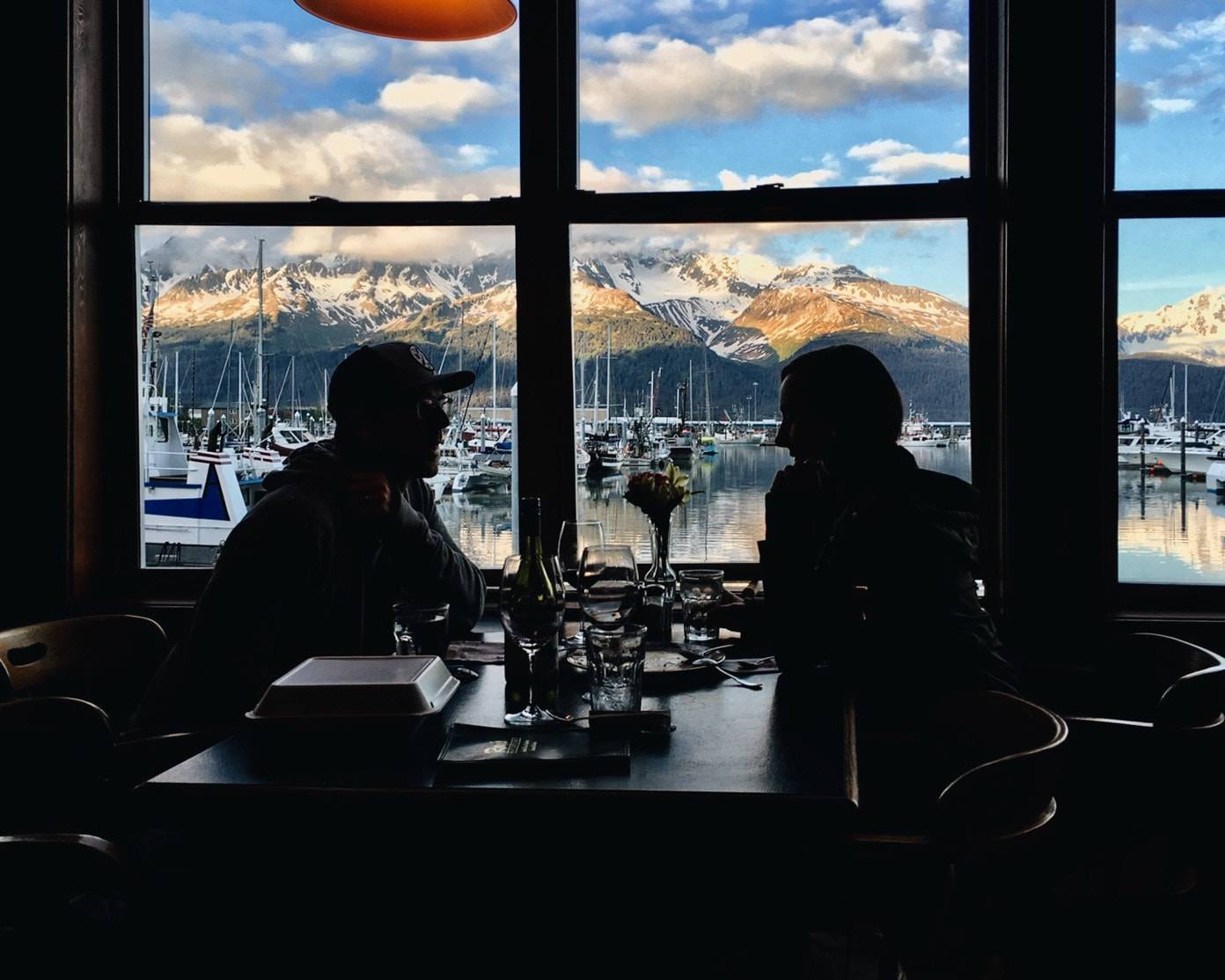 Two men next to a window sitting at a table.