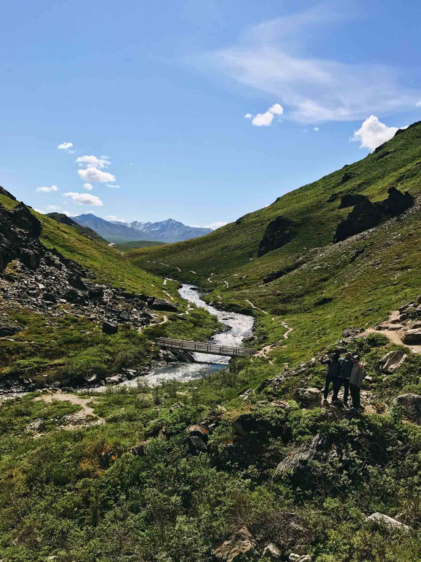 Mountains and grassy hills with a small bridge over a river.