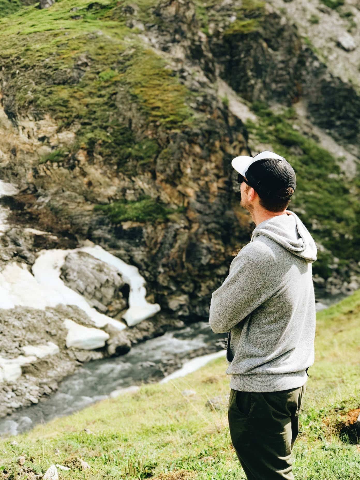 Man wearing a hat looking at grassy mountains.