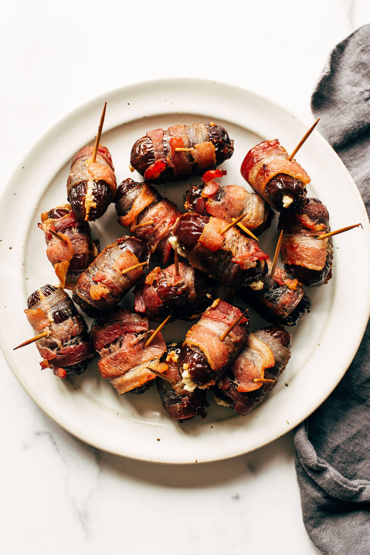 Bacon-wrapped dates on a plate with toothpicks in the dates.