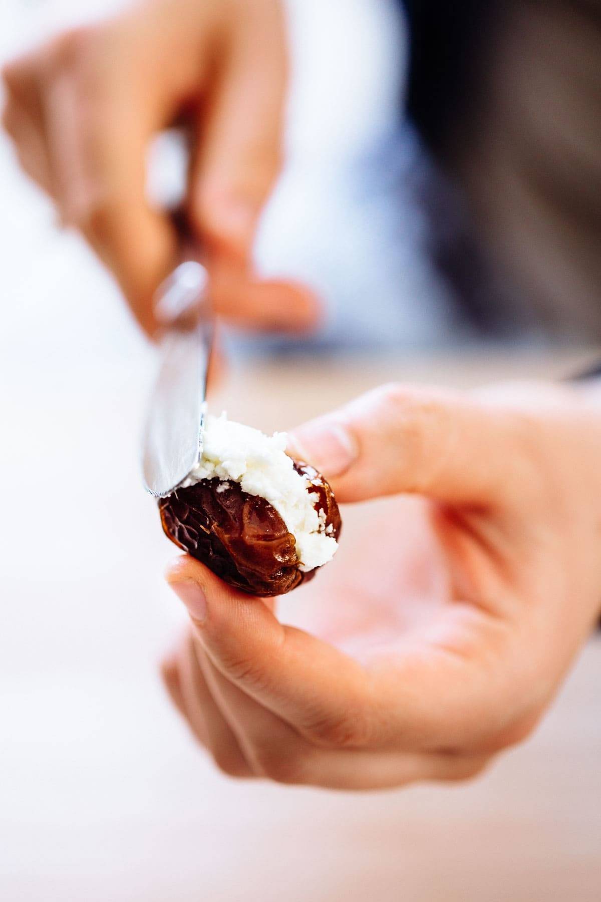 White hand filling date with goat cheese using a butter knife.