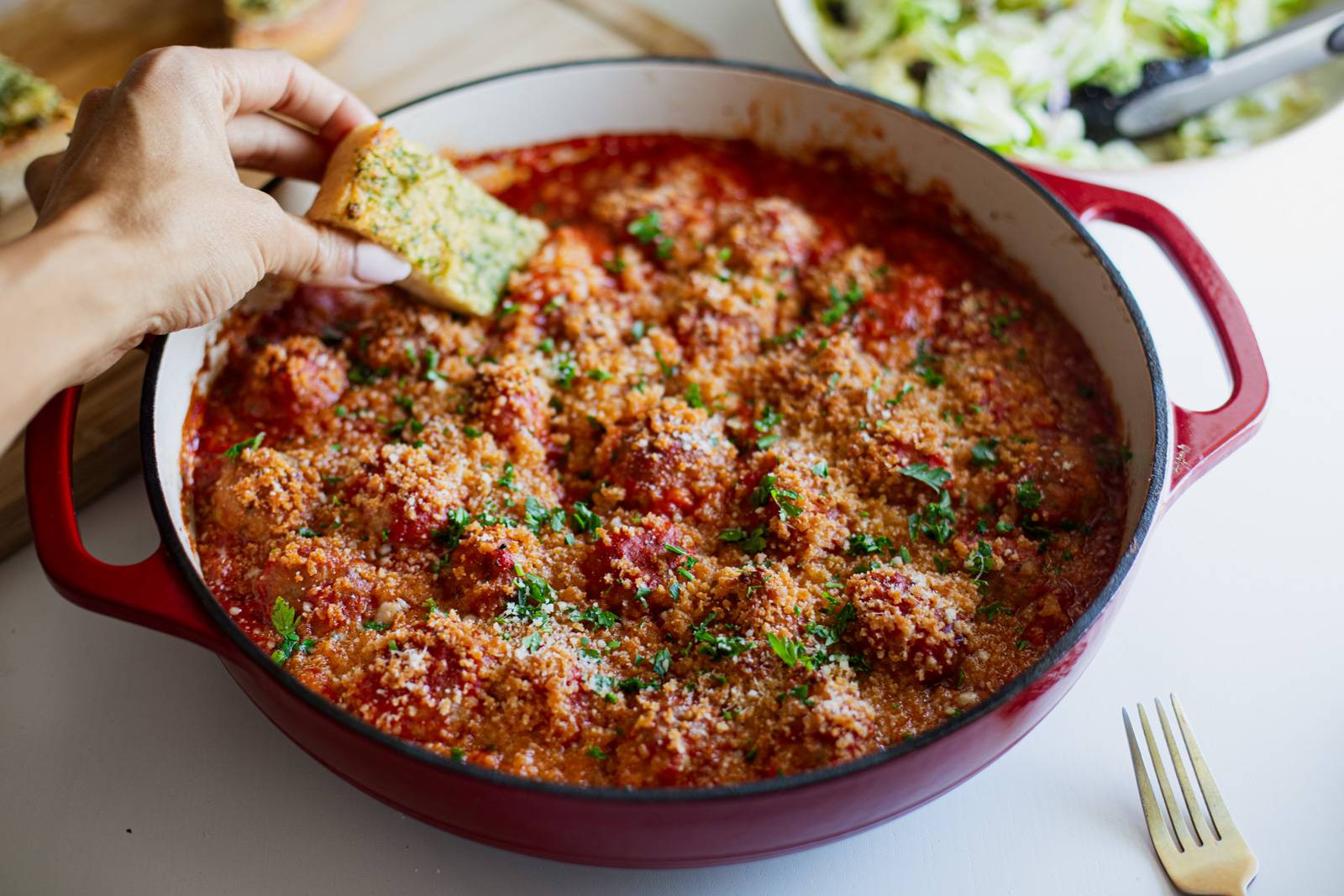 Dipping garlic bread into a pan of meatballs.