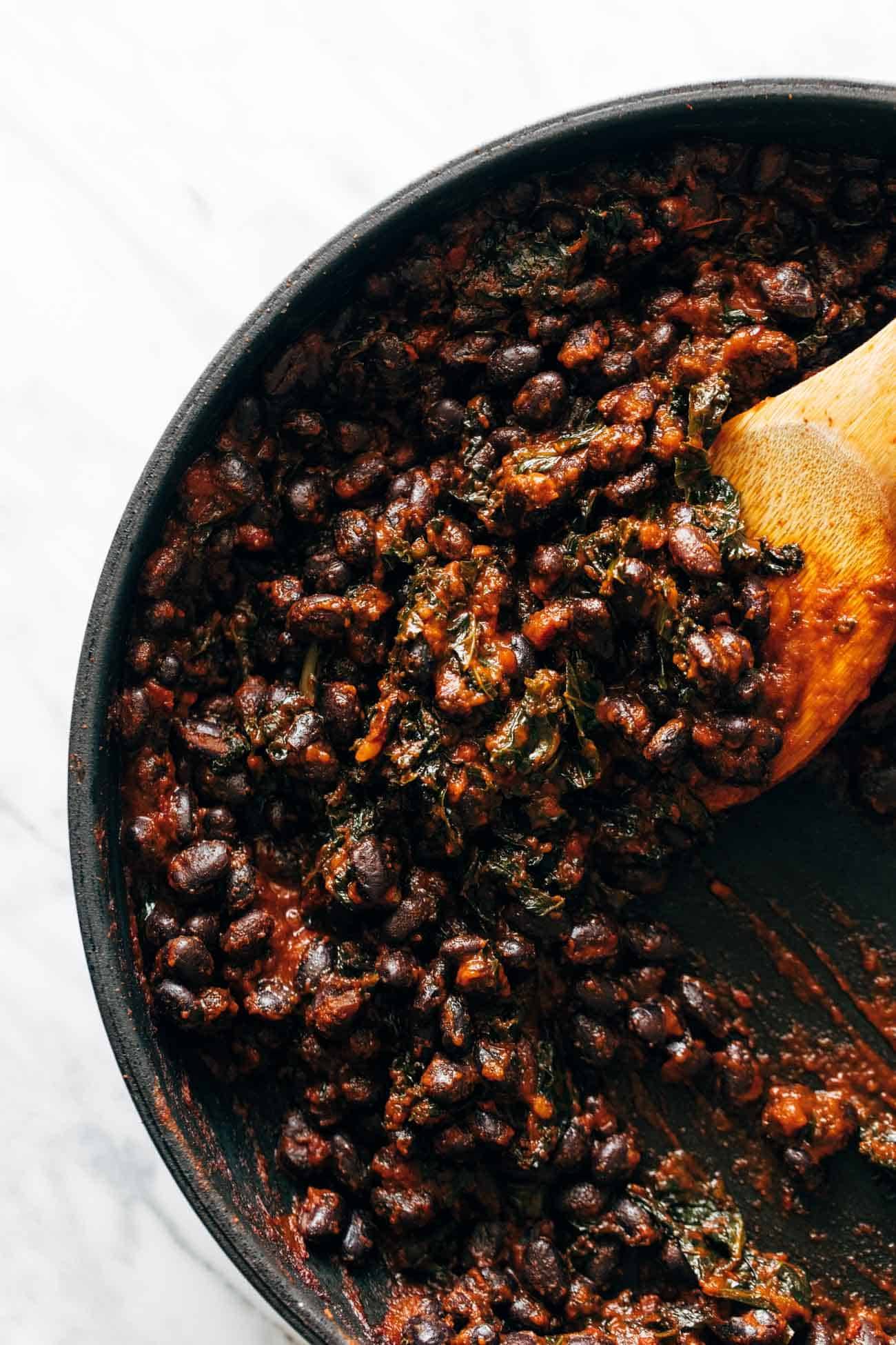 Smoky black bean filling with greens being stirred around in a pan with a wooden spoon. 