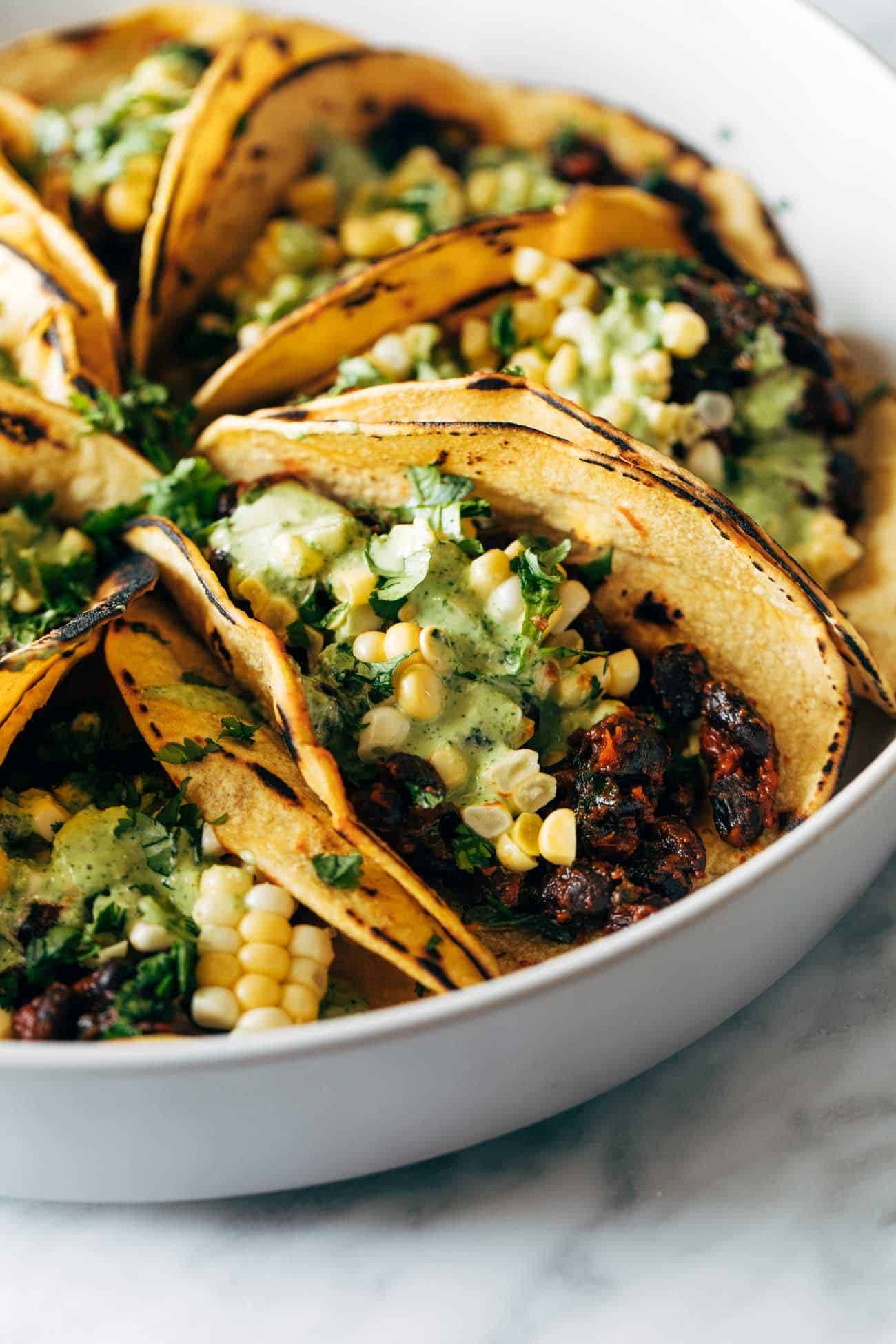 Close-up of Smoky Beans and Green tacos on a plate with corn and Aji verde sauce drizzled on top. 