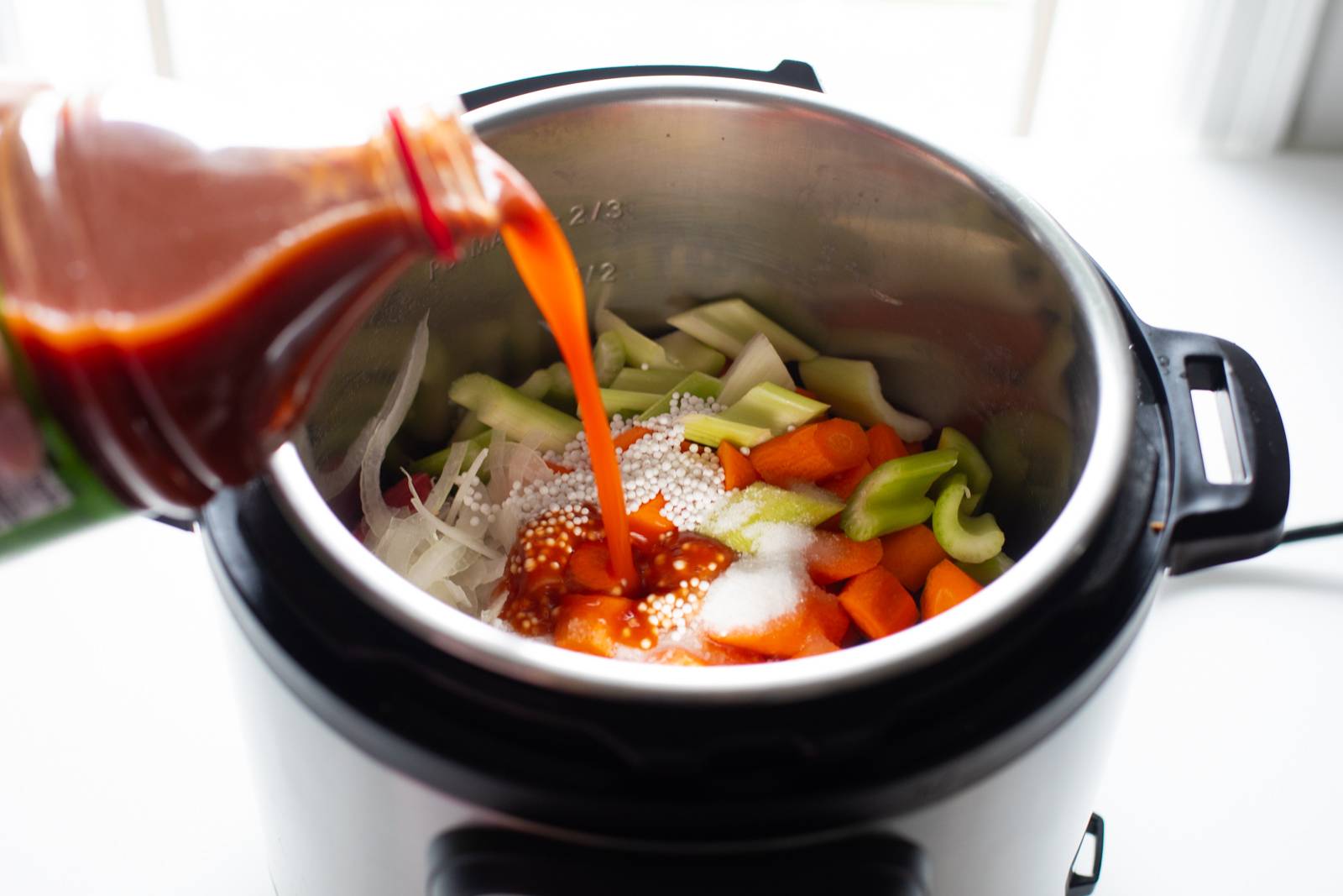 Pouring tomato juice into a pot of beef stew.