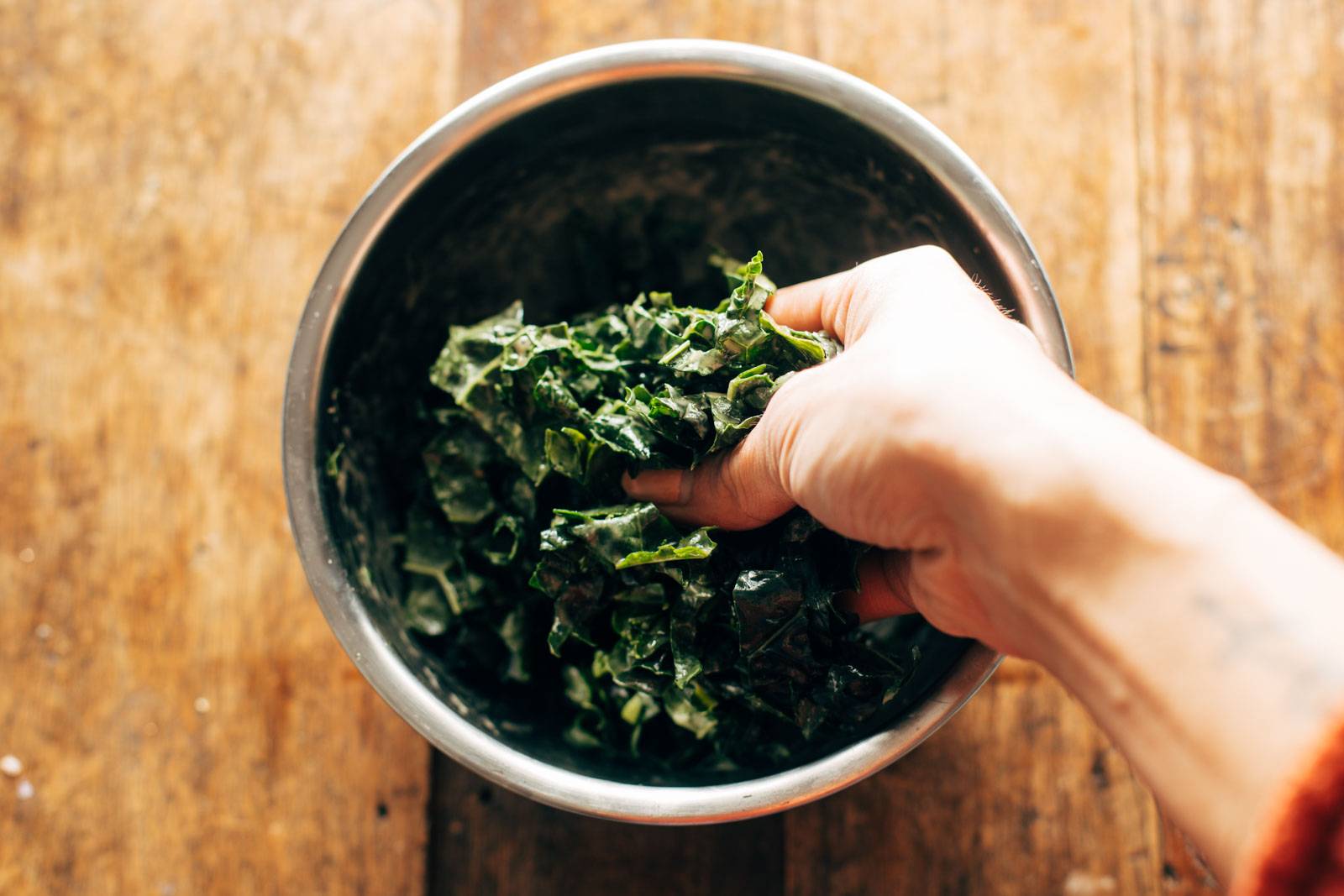 Hand massaging kale with dressing.