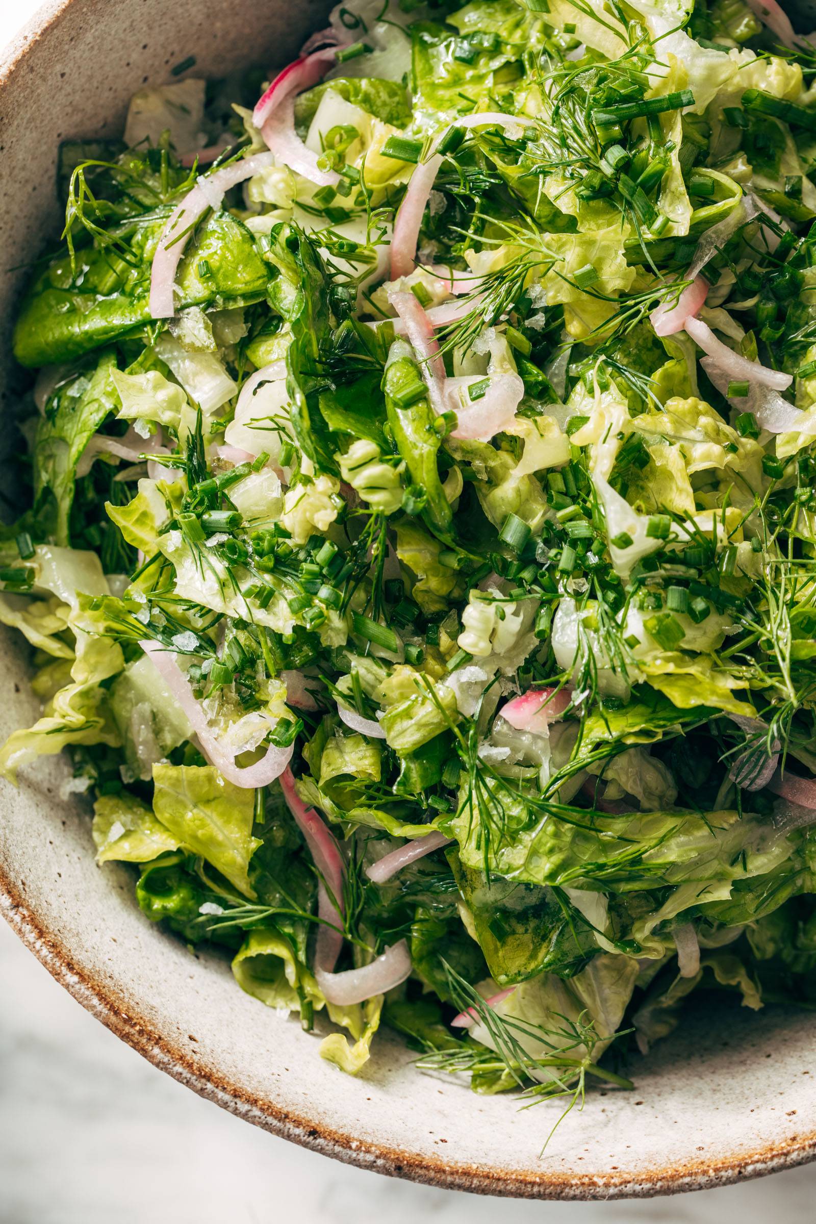 Salad with lettuce, fresh herbs, and pickled onions in a bowl.