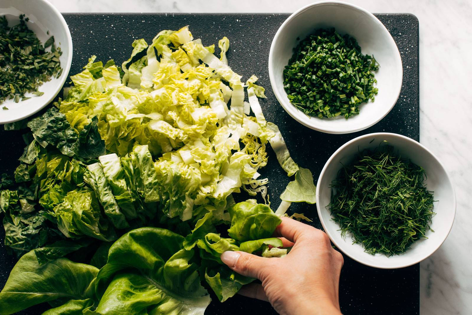 Chopped veggies and herbs on a cutting board.