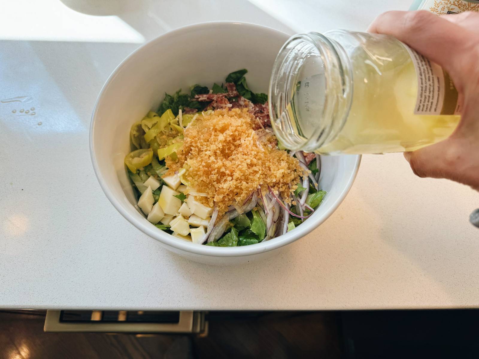 Pouring pepperoncini brine into a bowl of salad.