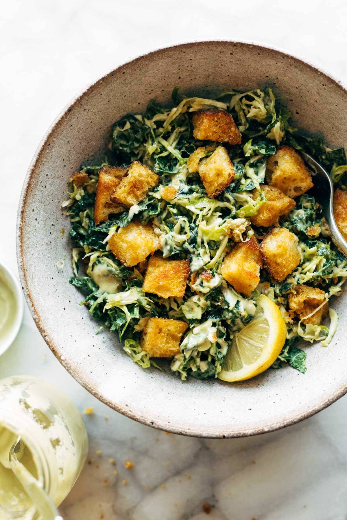 Brussels & Kale Caesar in a bowl with Cheezy Garlic Croutons.