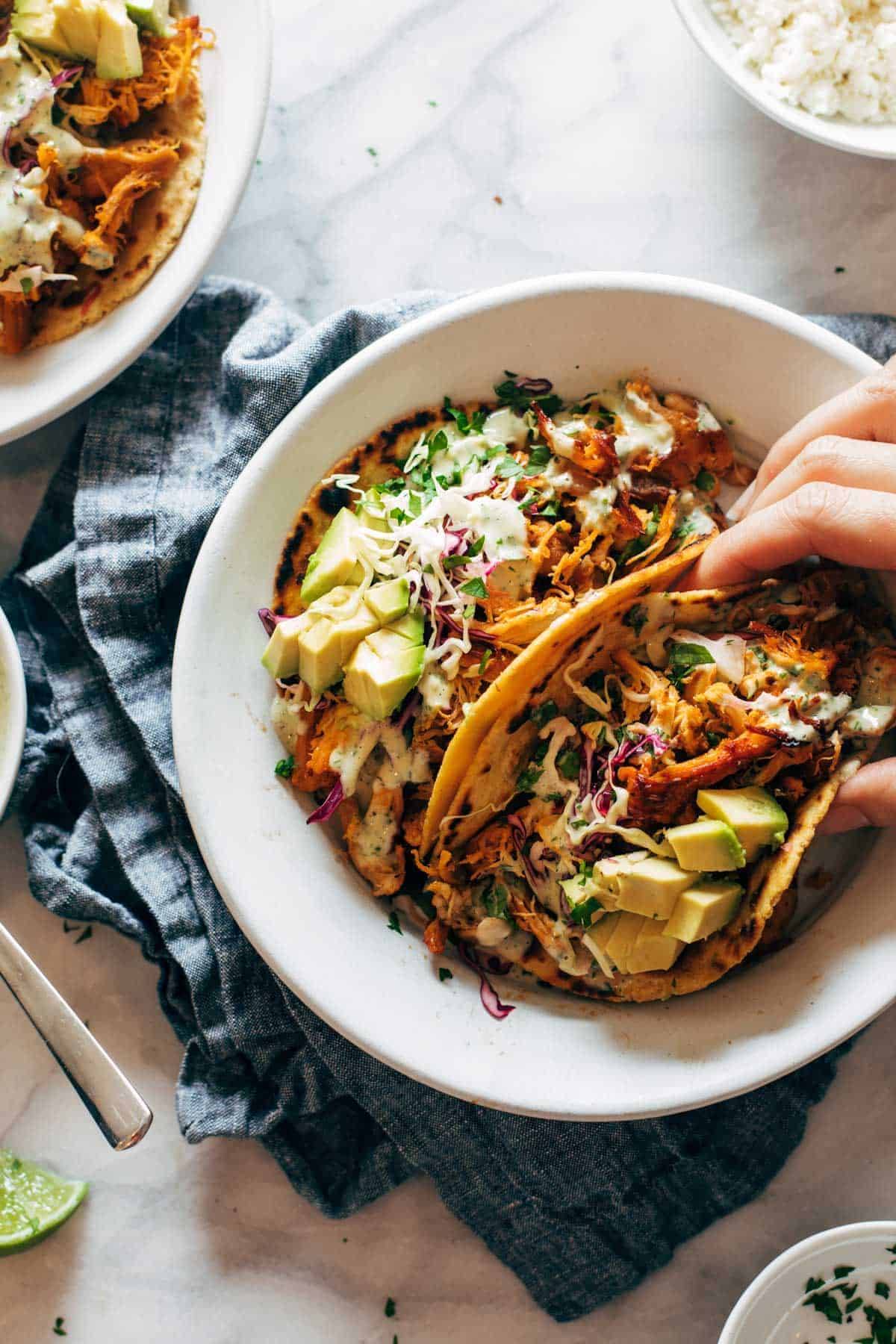 Hand grabbing buffalo chicken taco on a plate.