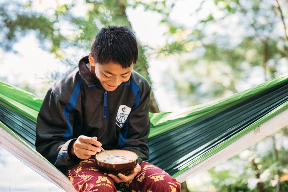 Boy eating in a hammock.