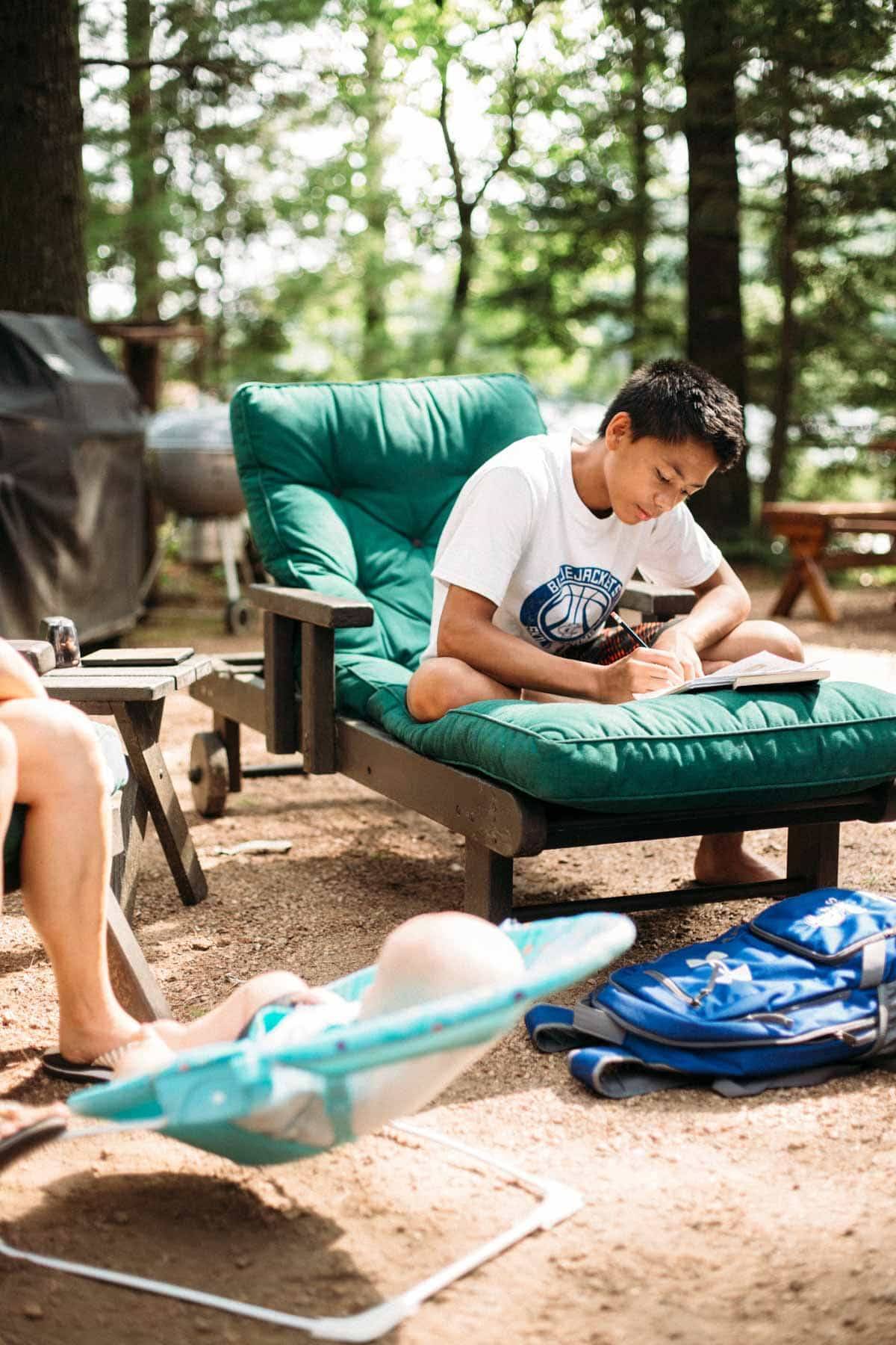 Boy sitting in a chair writing in a notebook.