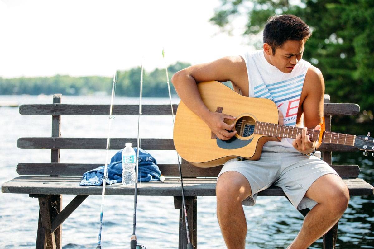 Boy playing guitar on a dock.