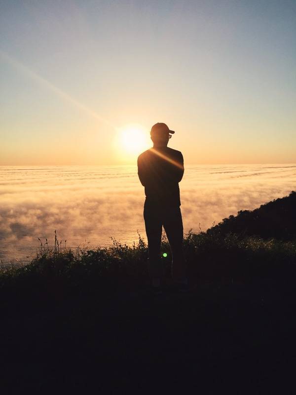 Man standing on a cliff looking at the sunset.