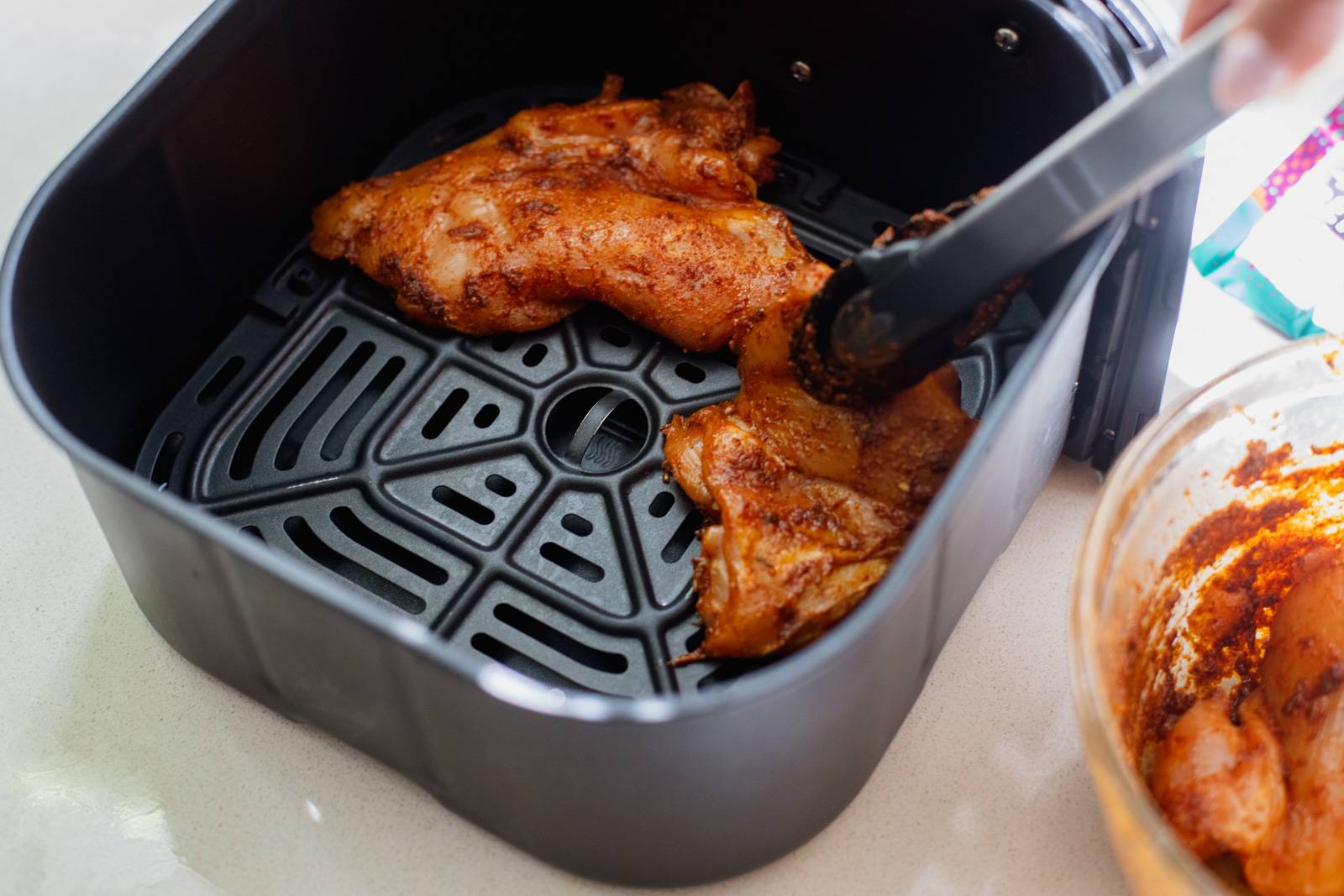 Adding raw chicken to an air fryer basket.