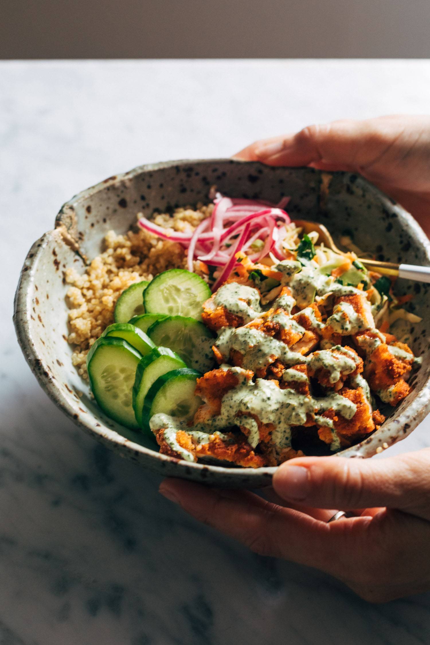 White hand holding a bowl of chicken tikka masala bowls with mint sauce on top