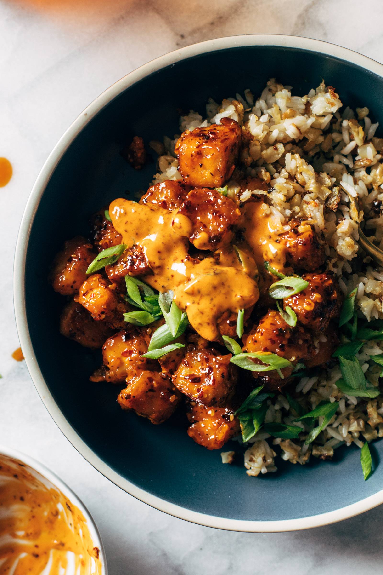 Chili crunch tofu in a bowl with sauce, rice, and green onions