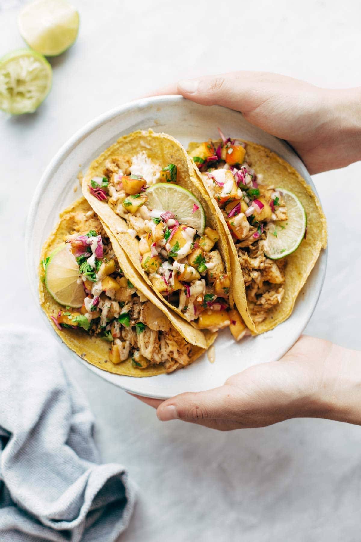 Hand holding a plate of chili lime fish tacos.