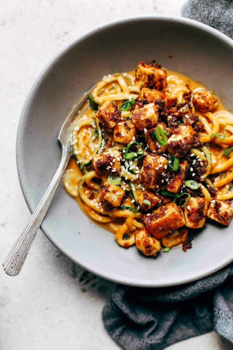 Zucchini noodles in a bowl with creamy sesame sauce and crispy tofu on top.