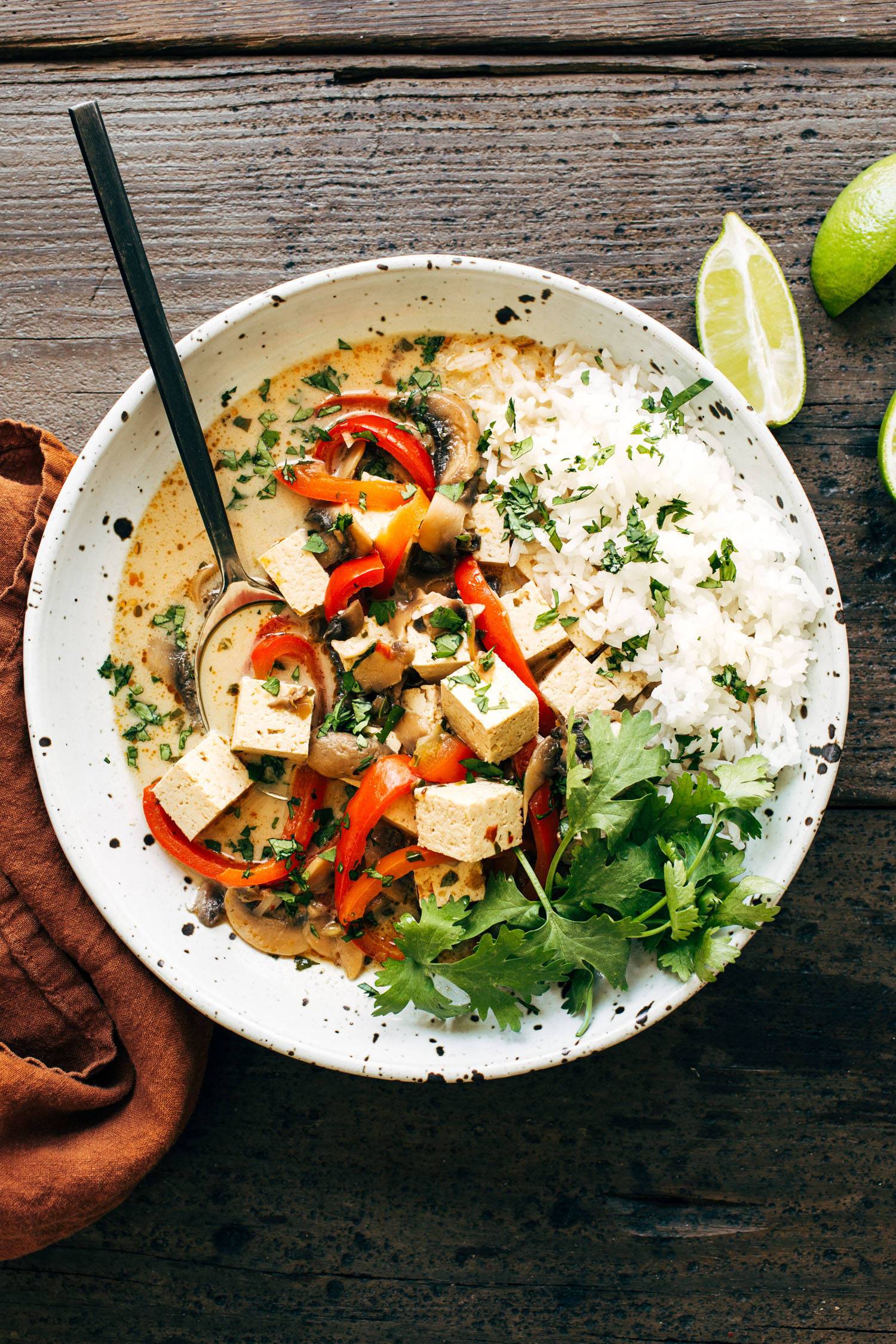 Thai coconut soup in a bowl with fresh cilantro, rice, tofu, and a spoon. 