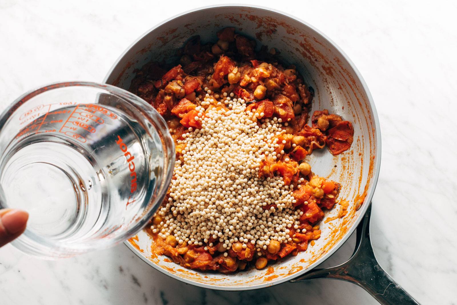 Adding pearled couscous to the pan.