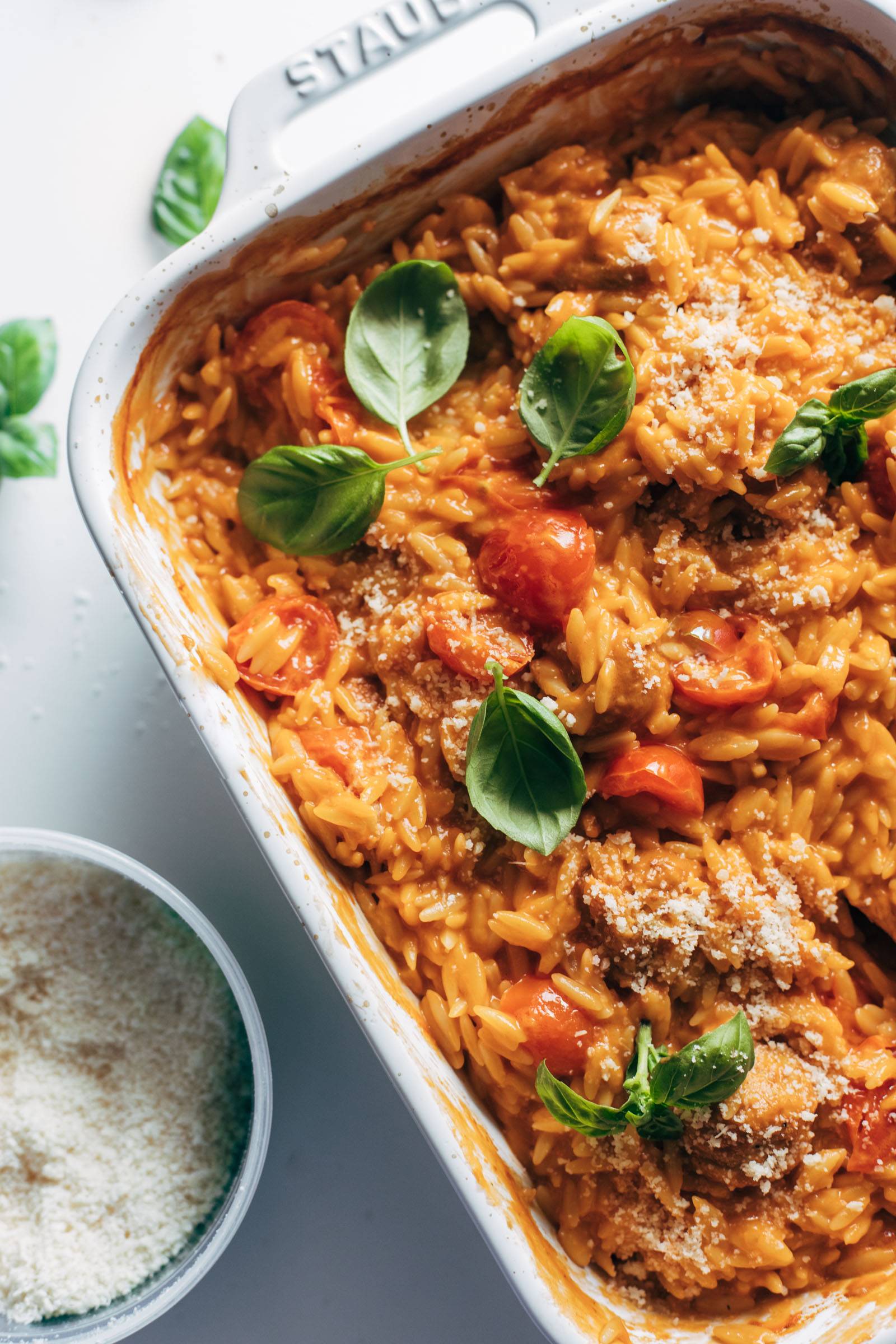 Creamy baked orzo in a pan next to a bowl of parmesan cheese