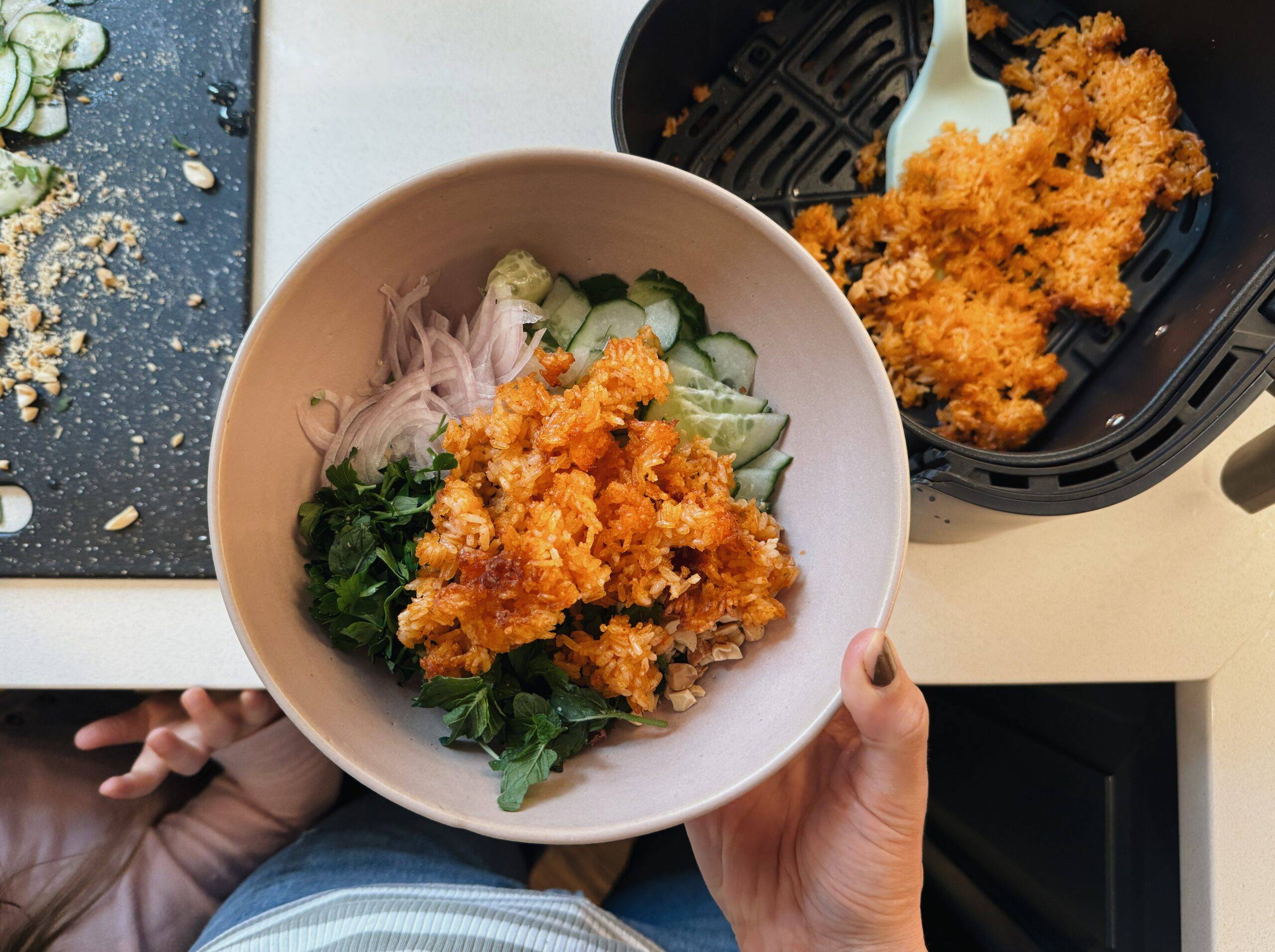 Hand holding a bowl of rice salad before mixing.