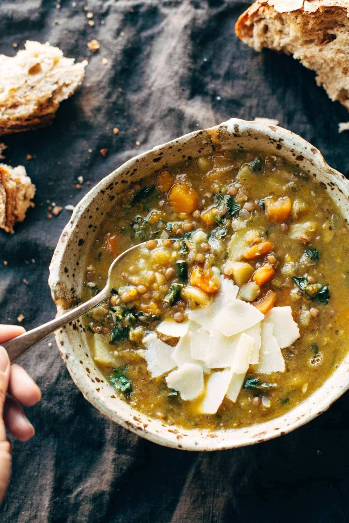 Crockpot lentil soup with cheese in a bowl with spoon and pieces of bread on the side.