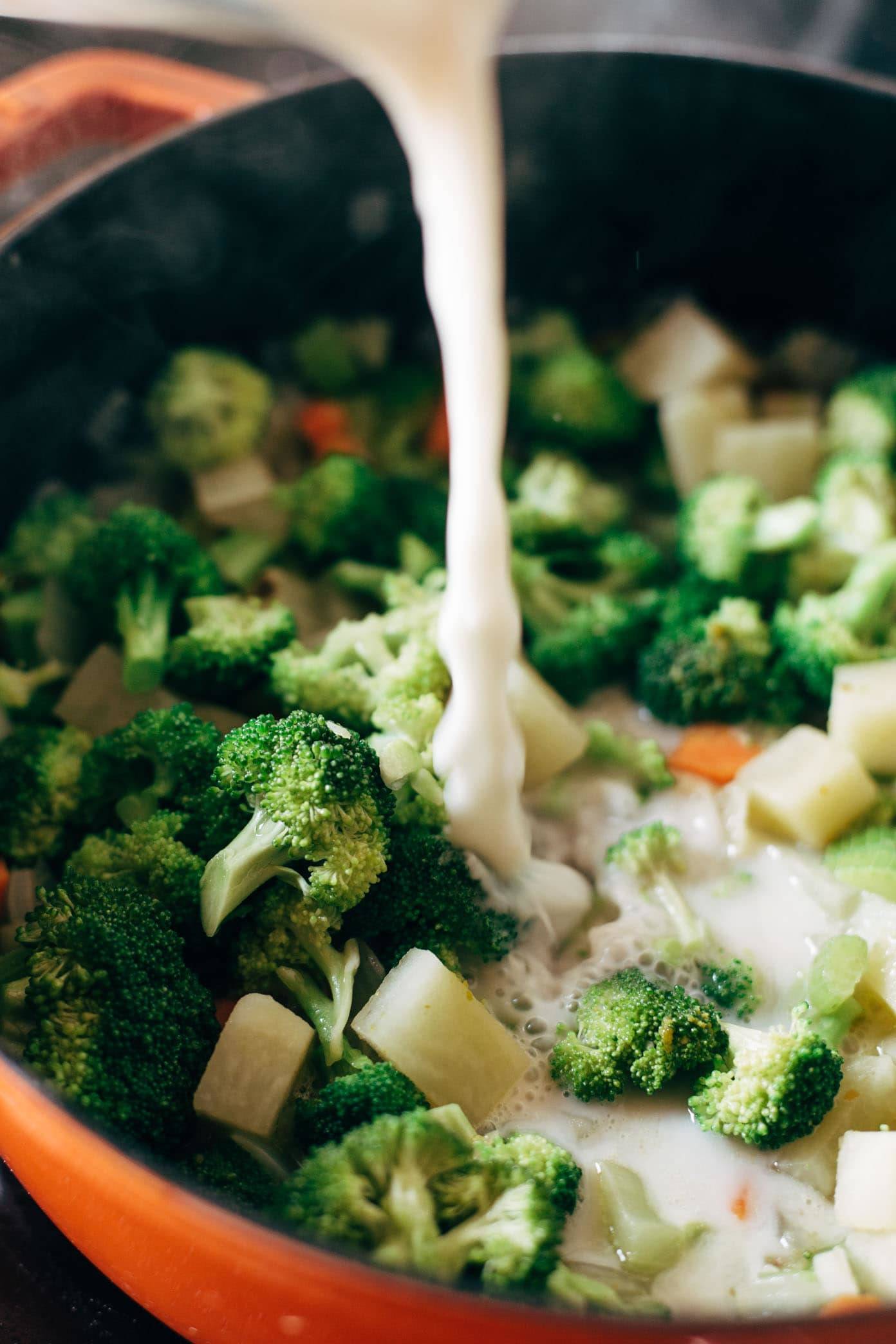 Pouring almond milk into vegan broccoli cheese soup.