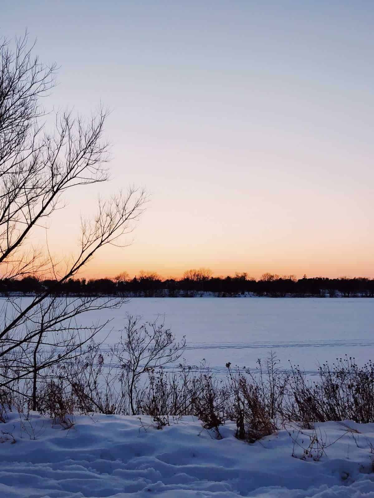 A winter scene with snow covering an empty field beneath a sky tinged with orange.