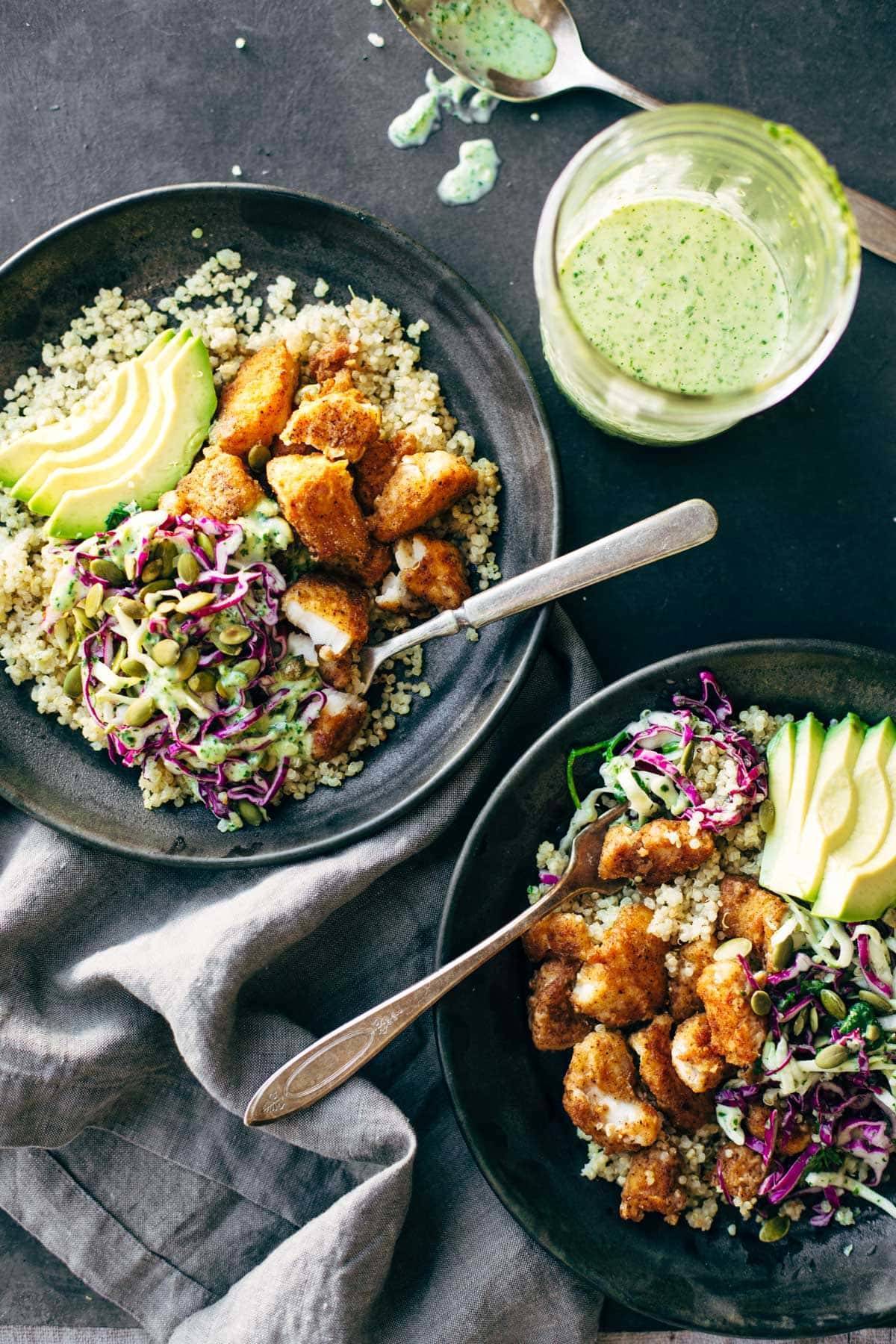 two fish taco bowls with cilantro lime slaw and jar of sauce with spoon