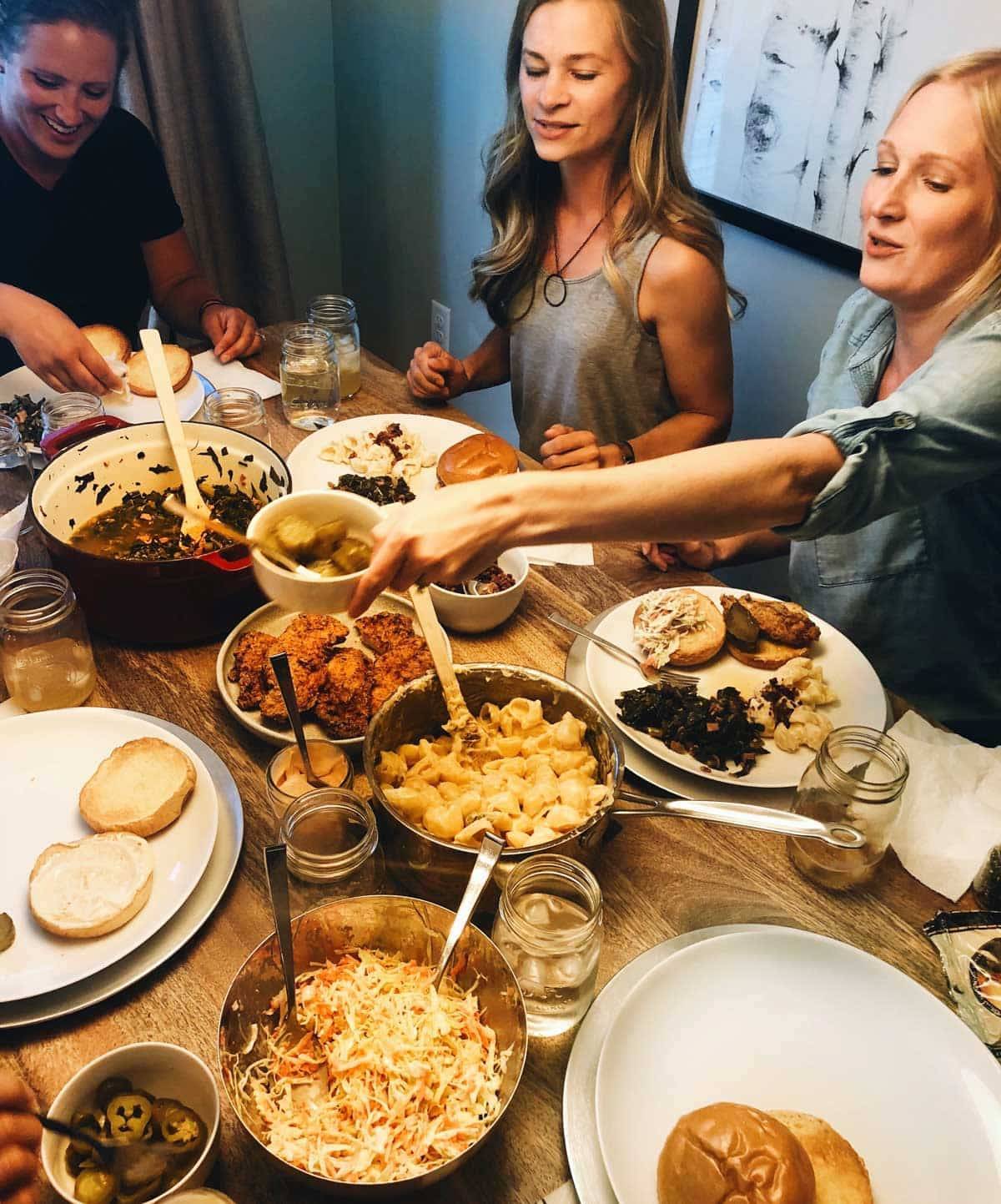 Guests enjoying fried chicken sandwiches, pasta, sauces and salads on a table.