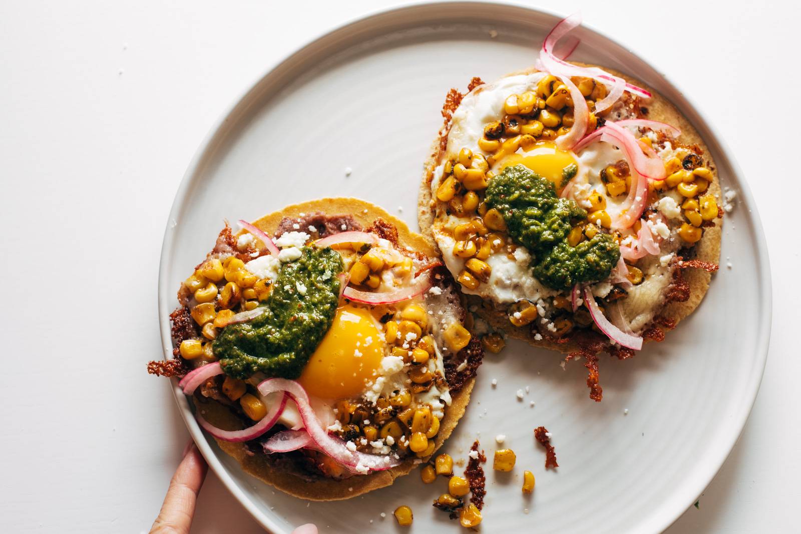 Two fried egg tacos on a plate with green sauce on top.