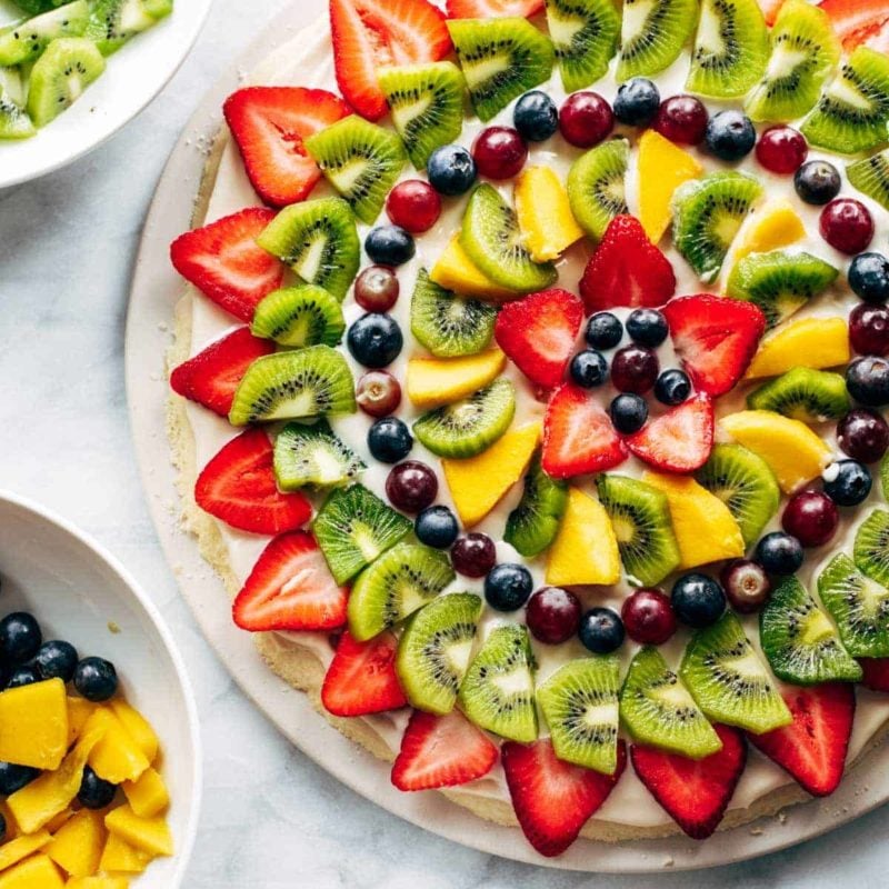 Fruit pizza with bowls of fruit.