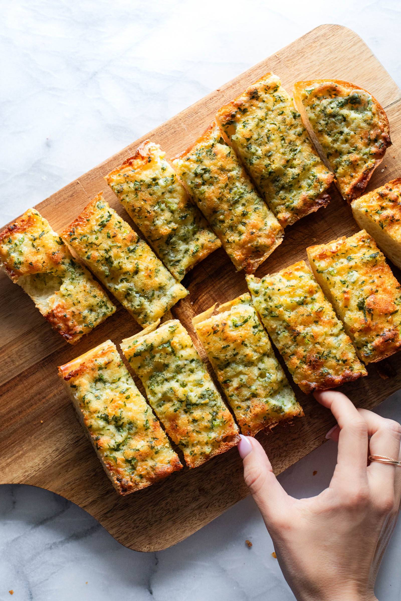 Hand grabbing a slice of garlic bread on a cutting board.