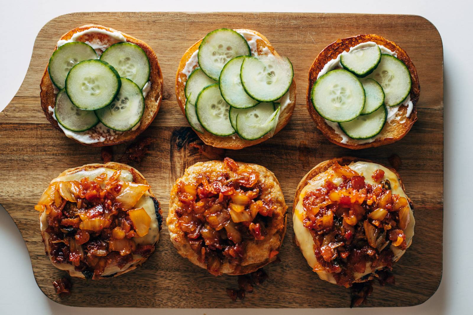 Cucumber slices and kimchi bacon jam being added to burgers