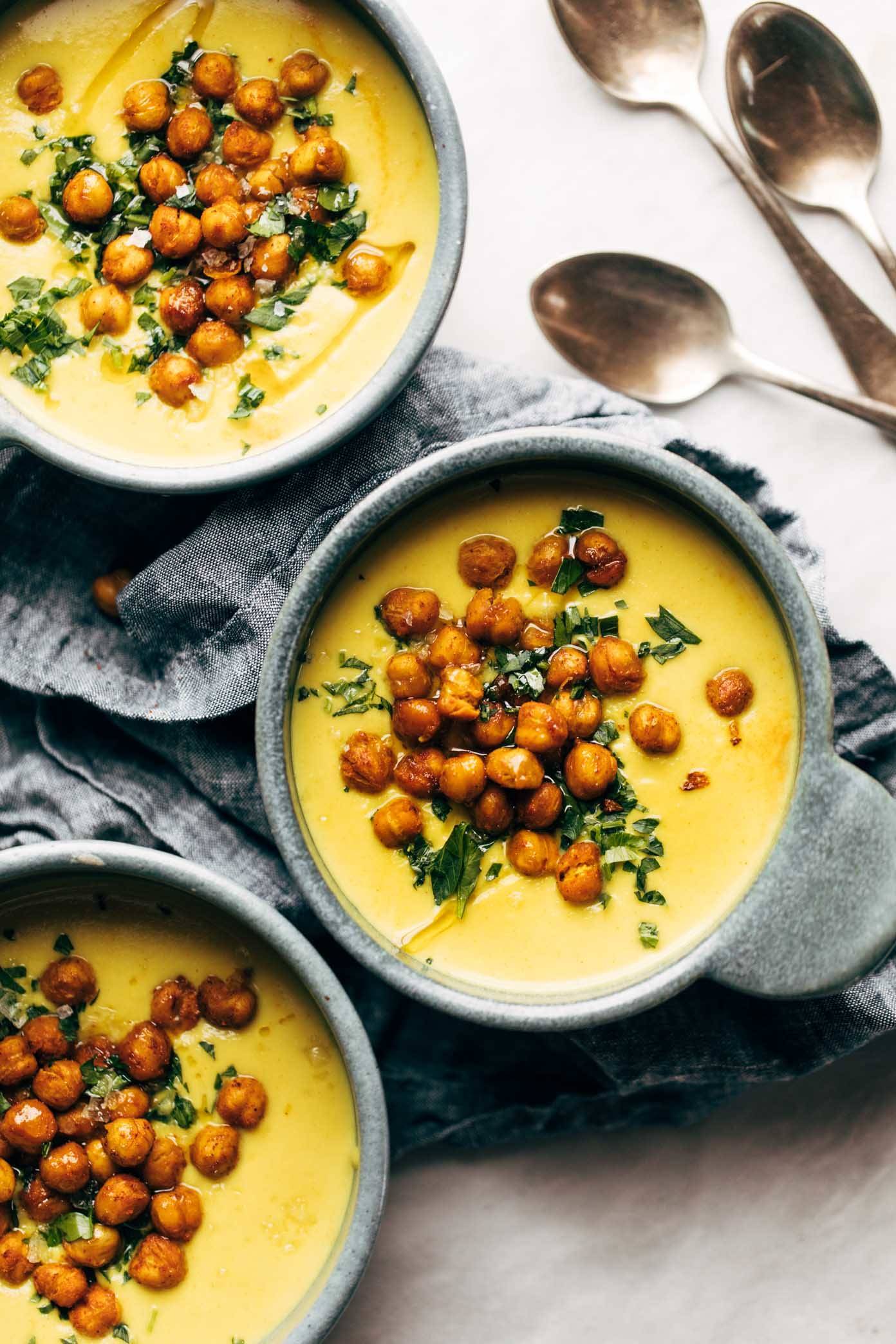 Three bowls of golden soup on a gray napkin next to three spoons.