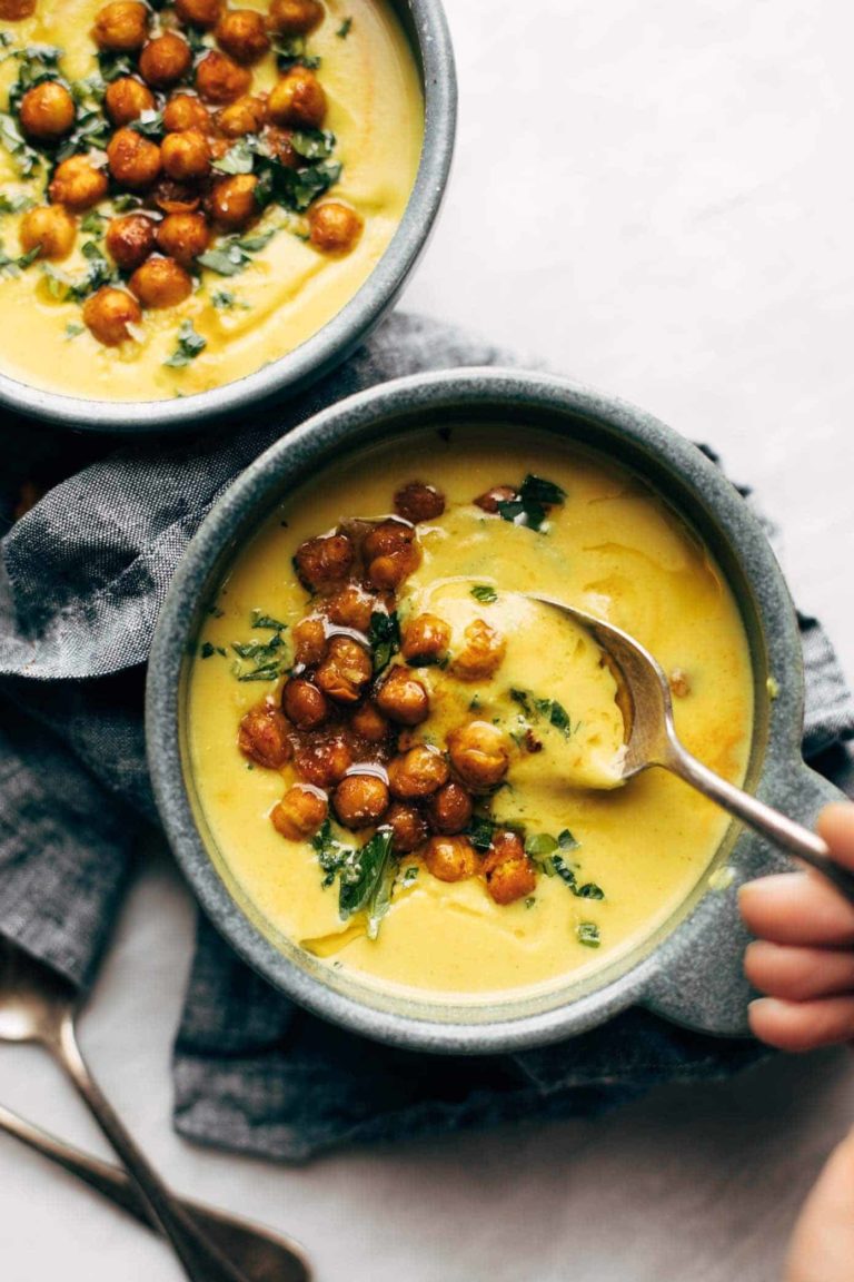 Two bowls of golden soup with roasted chickpeas and olive oil drizzled on top.