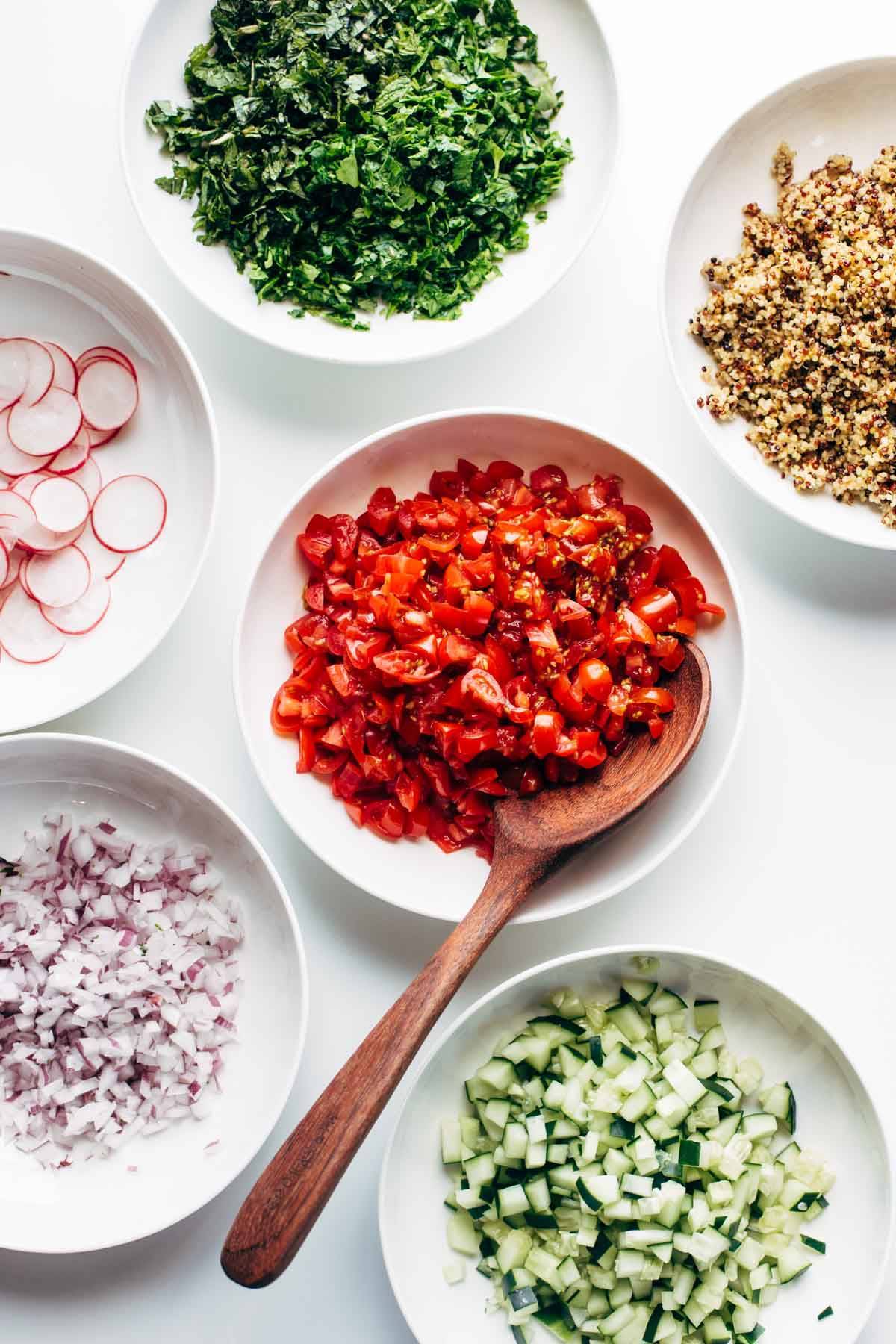 Salad ingredients in bowls with a wooden spoon.