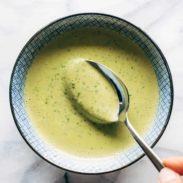 A spoon being dipped into green tahini sauce.