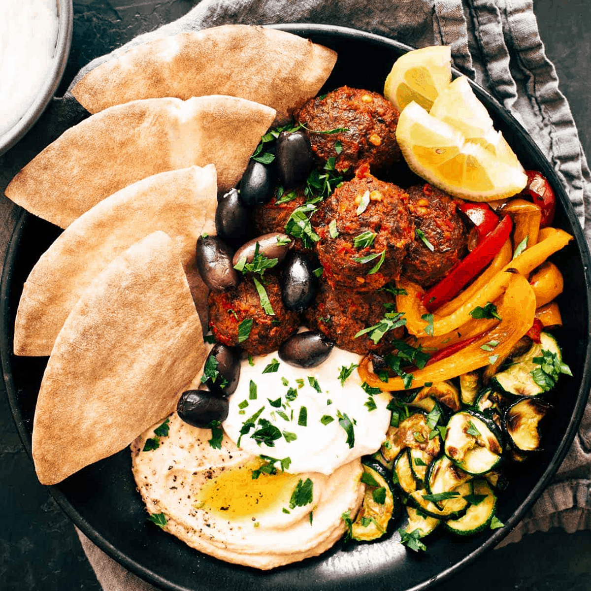 Harissa meatballs in a bowl with zucchini, peppers, olives, and hummus.