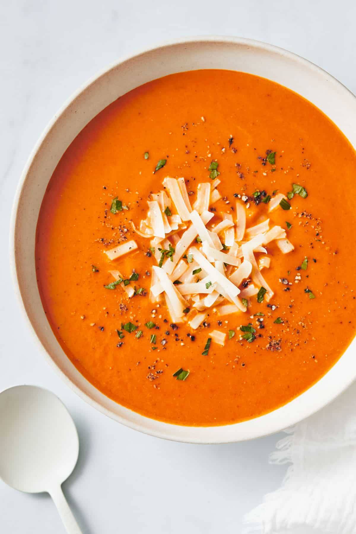 Tomato soup in a bowl in a white bowl with a white spoon. 