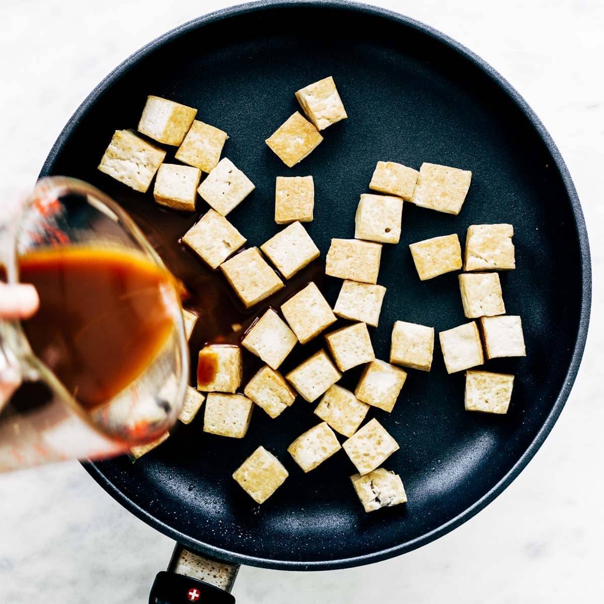 Pouring sauce on tofu in a sautè pan.