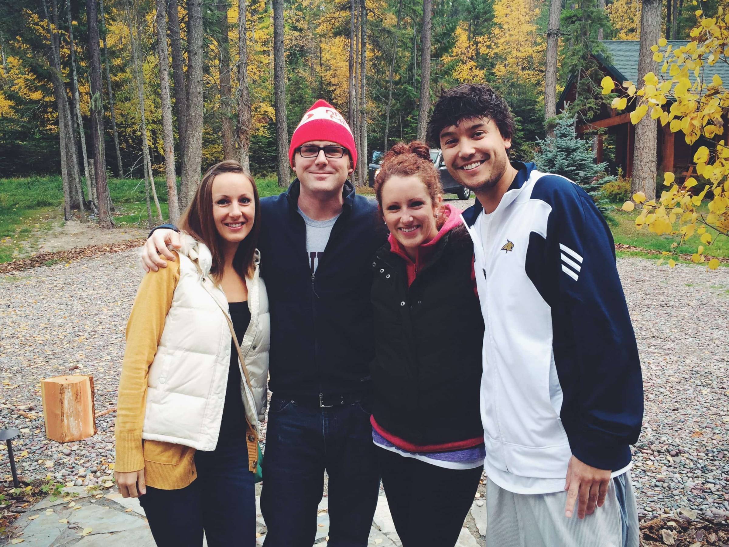 A group of four younger people standing and posing for a picture in front of trees.