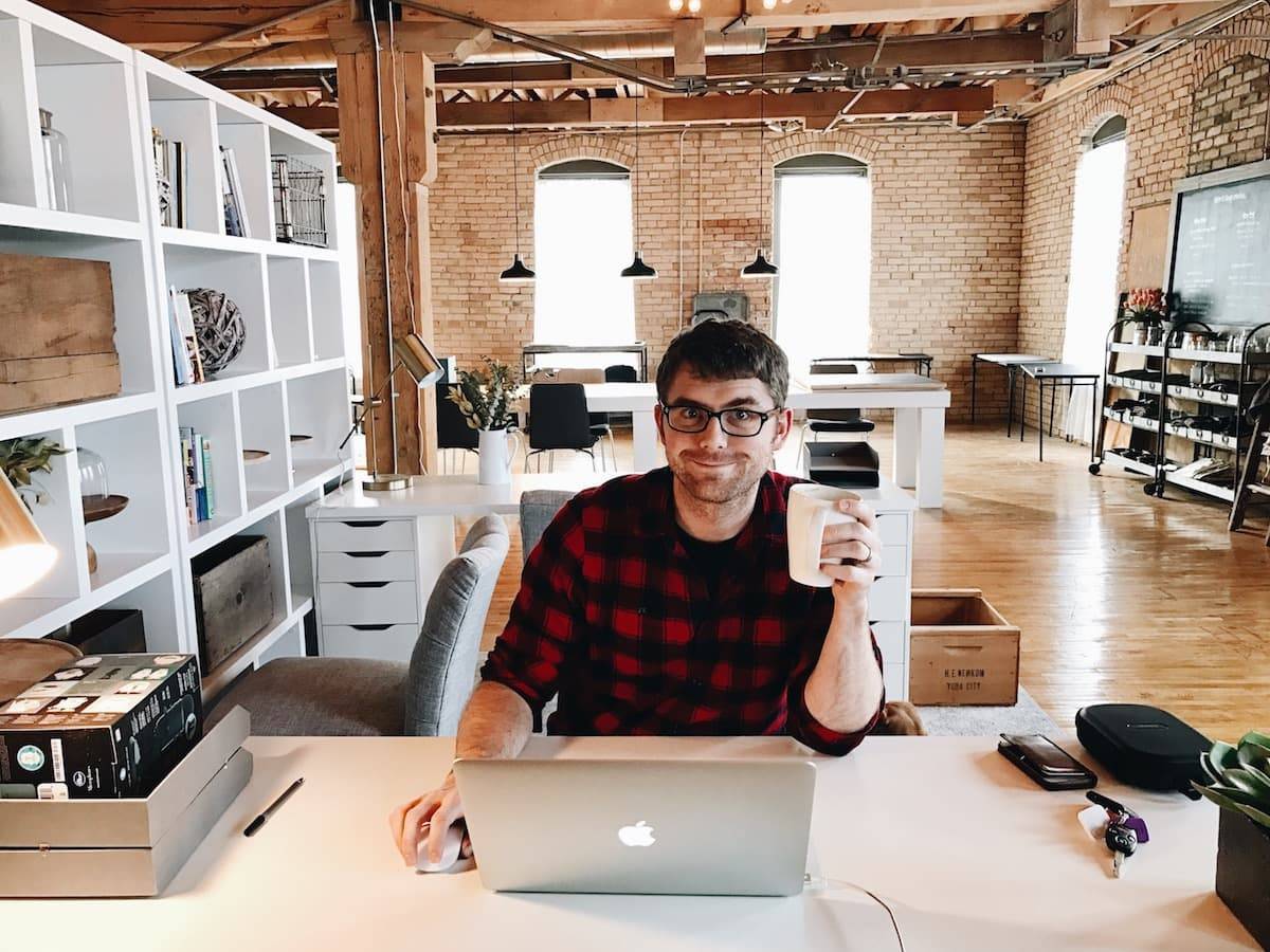 A man sitting in front of a laptop on his work desk holding a cup of coffee.