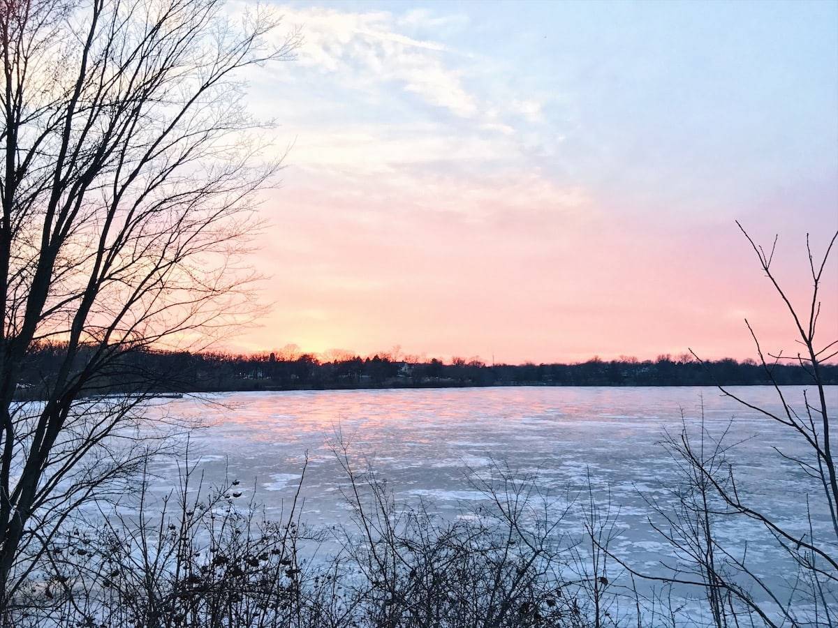 Sunrise with reddish and cloudy sky and large lake of water.